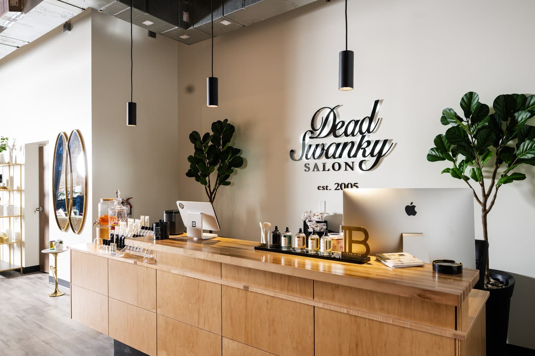 The salon's front desk in pale wood, with pendant lights, oval mirrors and the Dead Swanky sign on the wall