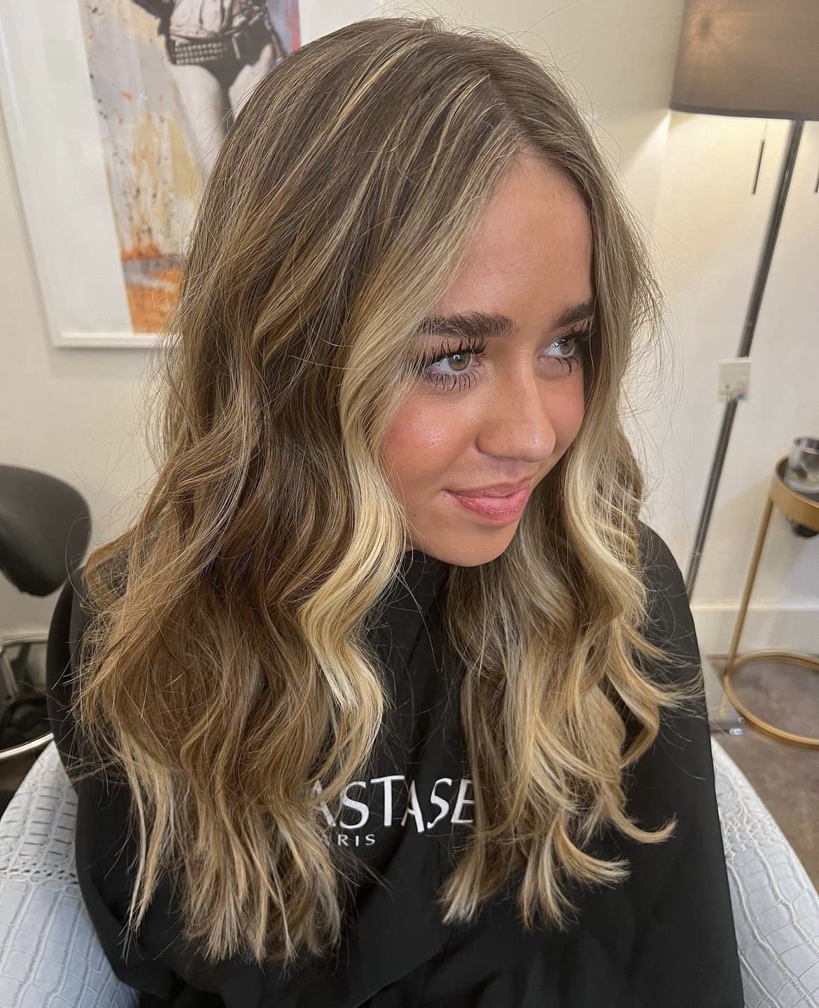 Bronde waves with soft, face-framing highlights on a smiling client in a Kérastase cape